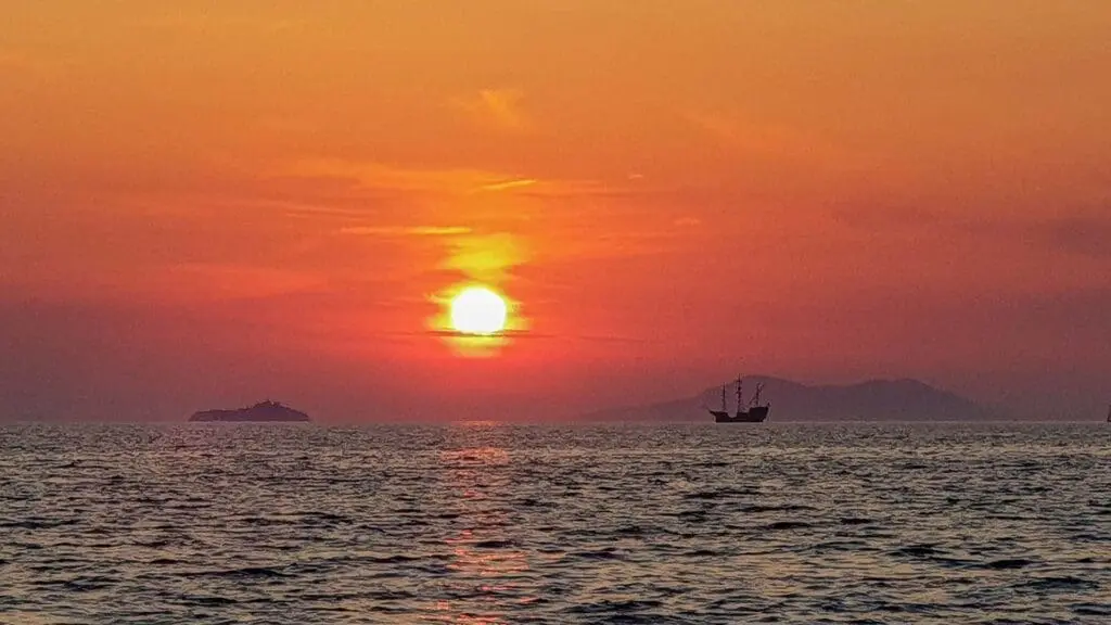 Sun setting over the ocean with a silhouette of a ship on the horizon and distant islands against an orange and red sky, reminiscent of idyllic private boat tours from Dubrovnik.