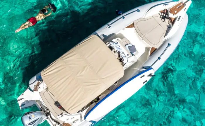 Aerial view of a person swimming near a white inflatable boat in the clear turquoise waters of Dubrovnik, perfect for private boat tours and day trips.