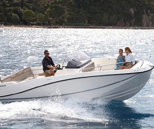 A man pilots a white motorboat on open water, with two passengers seated in the back. The shoreline with trees and hills is visible in the background—a perfect setting for private boat tours in Dubrovnik.