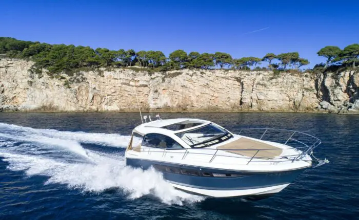 A motorboat speeds across the water near a rocky coastline with trees under a clear blue sky, perfect for Dubrovnik private boat tours.