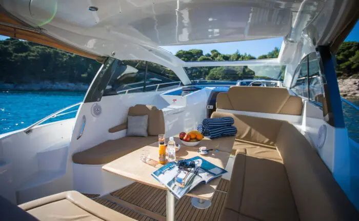 Experience the interior of a motorboat on one of our Private Boat Tours in Dubrovnik, featuring a table with snacks and drinks, cushioned seating, and towels. Enjoy the serene view of trees reflecting on the calm water during your relaxing day trip.