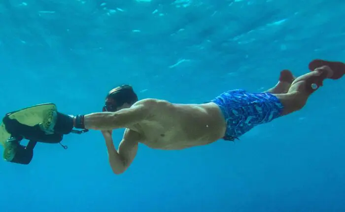 A person wearing blue shorts and swim fins is underwater in Dubrovnik, holding a dive scooter and swimming.