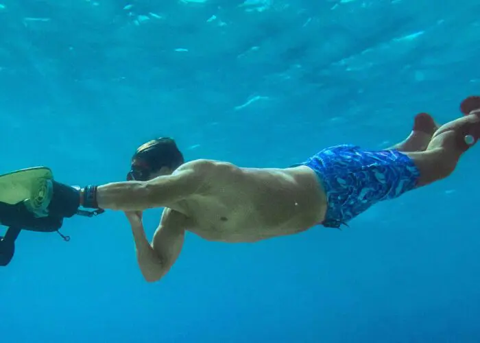 A person wearing blue shorts and swim fins is underwater in Dubrovnik, holding a dive scooter and swimming.