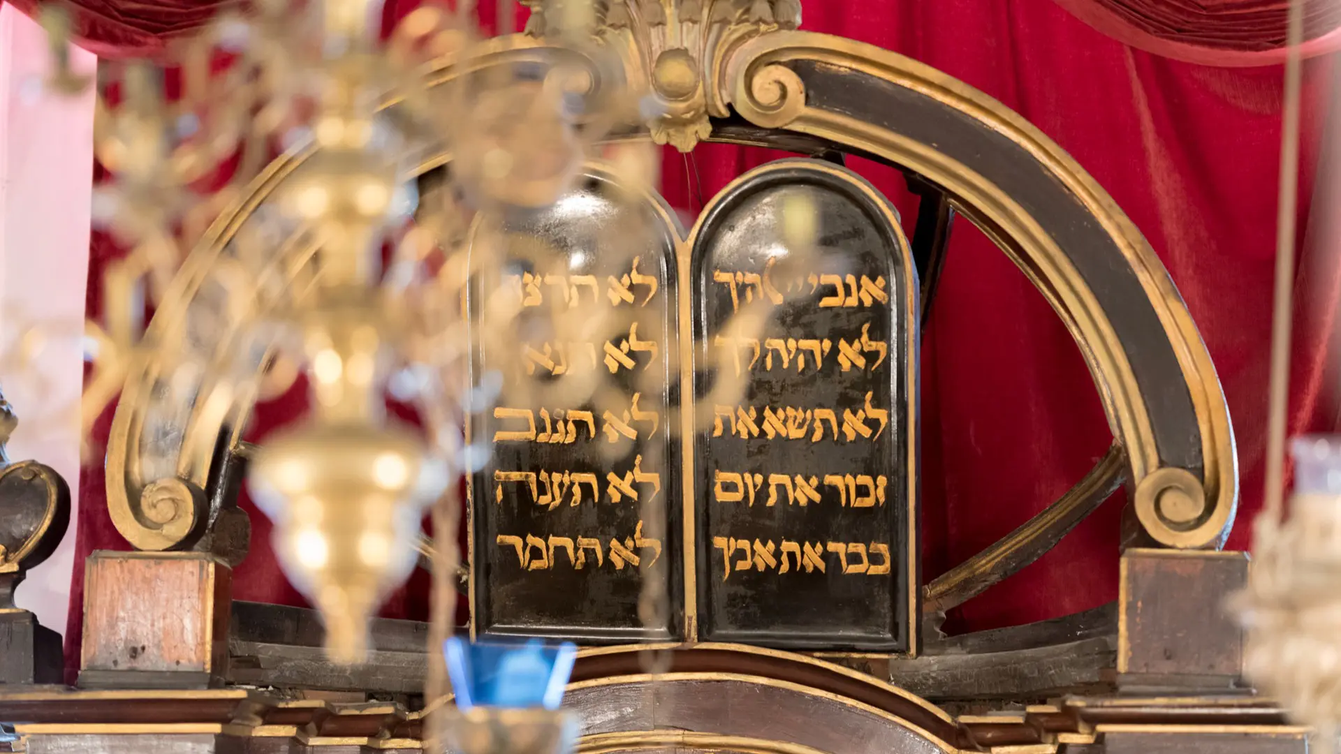 Tablets with Hebrew script are elegantly displayed in an ornate, classical setting, adorned with red drapery and golden accents, capturing the essence of Dubrovnik’s Jewish legacy.