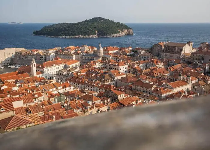 Aerial view of Dubrovnik's coastal town with orange-tiled rooftops by the sea, an island visible in the distance—perfect for private boat tours or day trips.