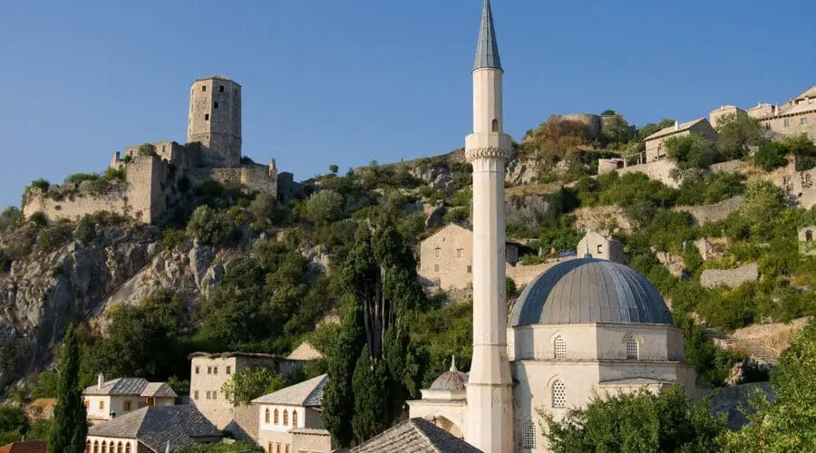 A historical hillside town resembling Dubrovnik, featuring a stone fortress, mosque with a tall minaret, and traditional buildings with red-tiled roofs under a clear blue sky. Ideal for day trips or private boat tours to explore its rich heritage and scenic beauty.