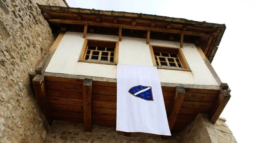 A white banner with a blue and yellow emblem, advertising day trips and private boat tours in Dubrovnik, hangs from a wooden balcony on a stone building.