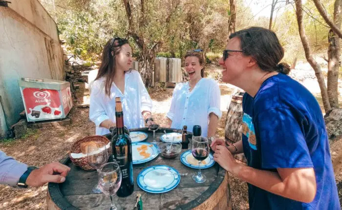 Three people enjoy a casual outdoor meal around a rustic barrel table in Dubrovnik, sharing wine and snacks while laughing together, reminiscent of the joy found on private boat tours or day trips.