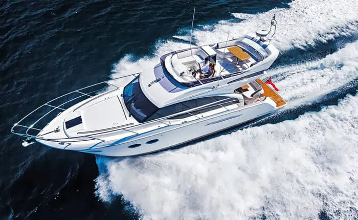 A white luxury yacht cruises through the blue ocean waters near Dubrovnik, leaving a trail of foam in its wake. Perfect for day trips and private boat tours, two people are visible on the top deck, enjoying the serene voyage.