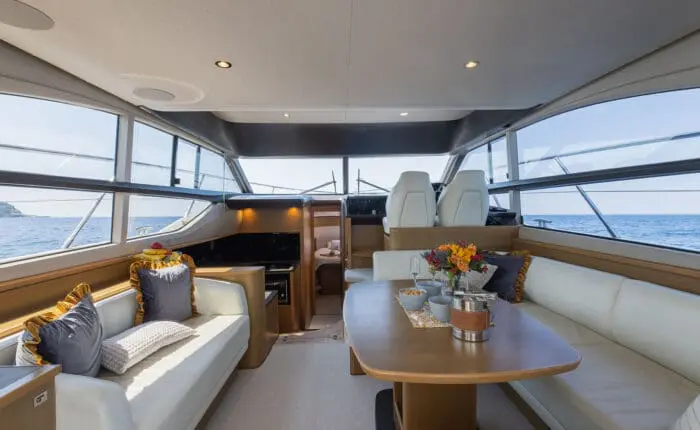 Experience a spacious yacht interior with modern furnishings, perfect for private boat tours in Dubrovnik. Enjoy a seating area, table adorned with flowers, and large windows offering an exquisite ocean view—a sublime setting for unforgettable day trips.