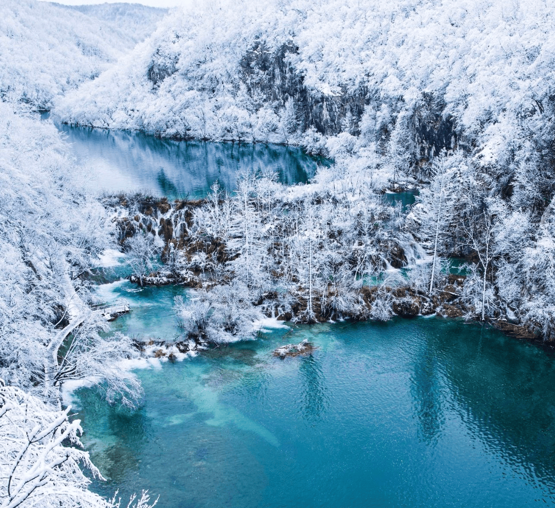 Snow-covered landscape with turquoise lakes and forested hills, captured from above.