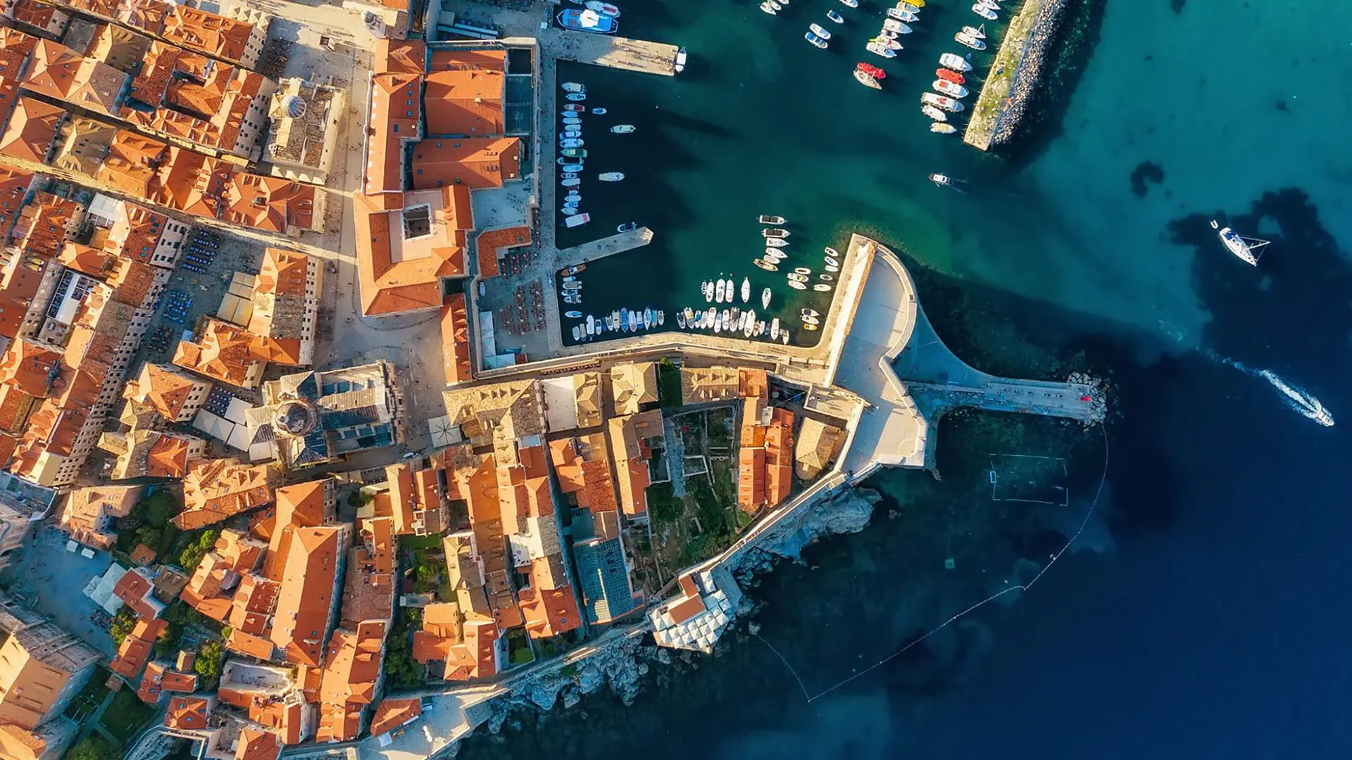 Aerial view of a picturesque coastal town in Croatia, with red-roofed buildings, a marina filled with boats, and crystal-clear blue water—a perfect spring destination for travellers seeking serenity and beauty.