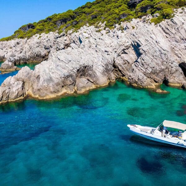 A private boat floats on clear blue-green water near rocky cliffs covered with lush vegetation, perfect for day trips from Dubrovnik.
