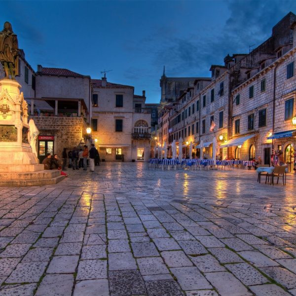 A cobblestone square in Dubrovnik, Croatia, at dusk with lit streetlamps, a statue, and surrounding historic buildings sets the stage for unforgettable day trips.
