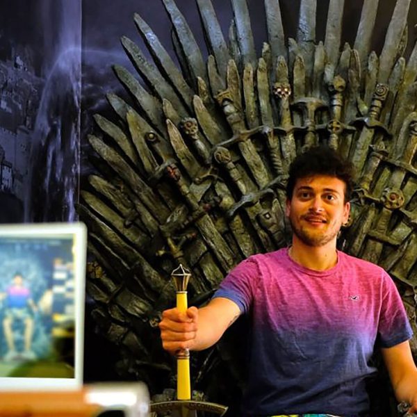 A person sits on a replica of the Iron Throne from "Game of Thrones," holding a sword while being photographed with a smartphone on a tripod, capturing the essence of Dubrovnik's iconic scenery.