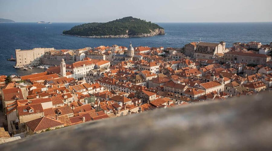 Aerial view of Dubrovnik's coastal town with orange-tiled rooftops by the sea, an island visible in the distance—perfect for private boat tours or day trips.