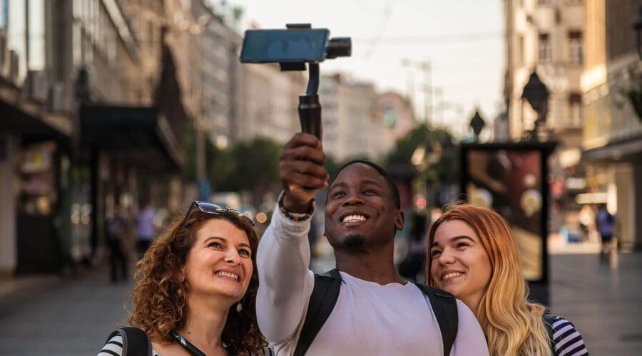 Three people smiling and taking a selfie with a smartphone on a gimbal in the bustling streets of Dubrovnik, capturing memories before their serene private boat tour.