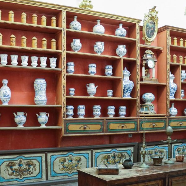 A historical apothecary shelf with blue and white ceramic jars and containers, some labeled, alongside wooden drawers and decorative accents, viewed from the front in a well-lit room—perfect for those interested in Dubrovnik day trips or private boat tours.