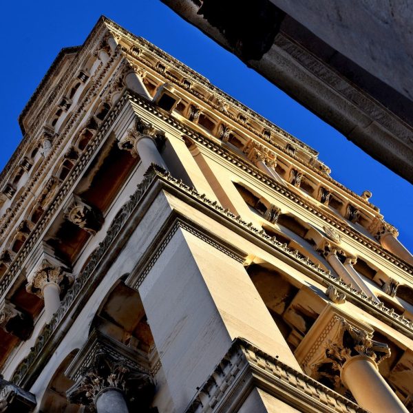 Upward view of an ornate, multi-story stone tower featuring columns and intricate carvings under a clear blue sky, reminiscent of the historic architecture seen in Dubrovnik.