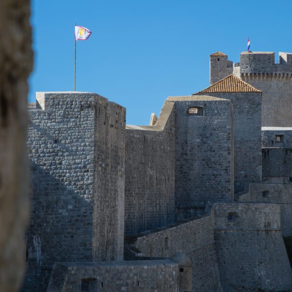 Historic stone fortress with tall walls and round towers under a clear blue sky, featuring a flag on the central tower—a perfect glimpse into your Dubrovnik Escape on a captivating 6-Day Tour.