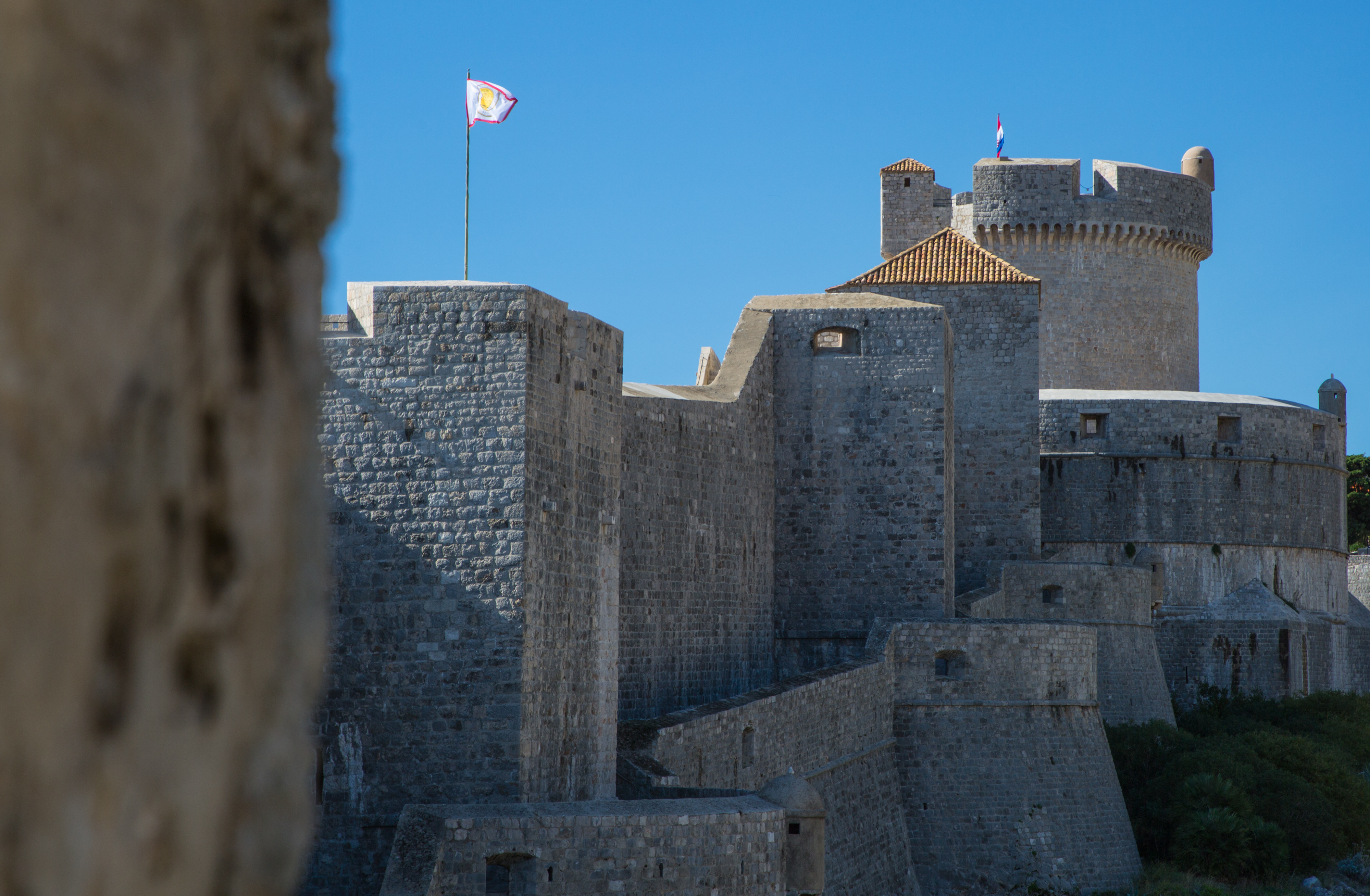 Historic stone fortress with tall walls and round towers under a clear blue sky, featuring a flag on the central tower—a perfect glimpse into your Dubrovnik Escape on a captivating 6-Day Tour.