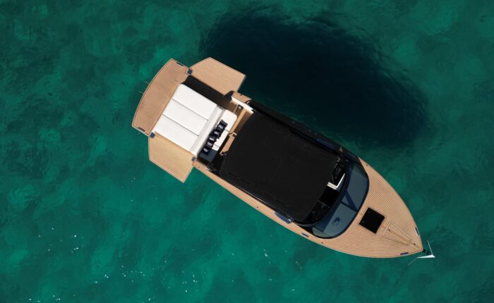 Aerial view of a wooden boat with a black canopy and white seating, floating in clear turquoise water near Dubrovnik. Perfect for private boat tours or day trips.
