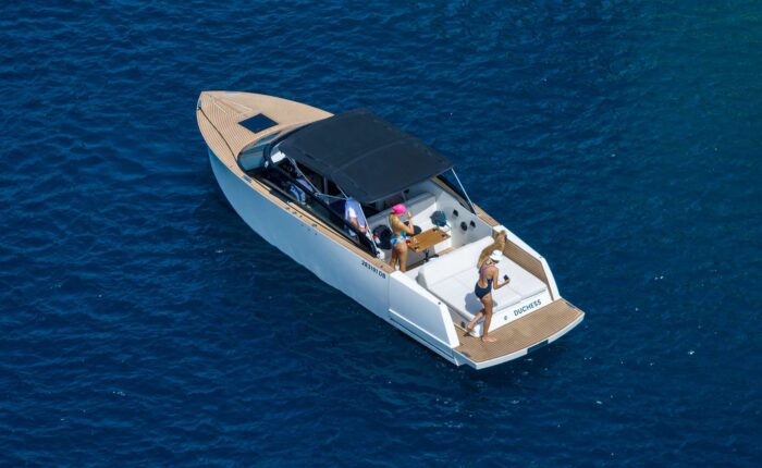 A white motorboat with a black canopy cruises on the deep blue waters near Dubrovnik. Three people are on board, engaging in various activities, enjoying their day trips. The boat is branded with "DRIECH," perfect for private boat tours.