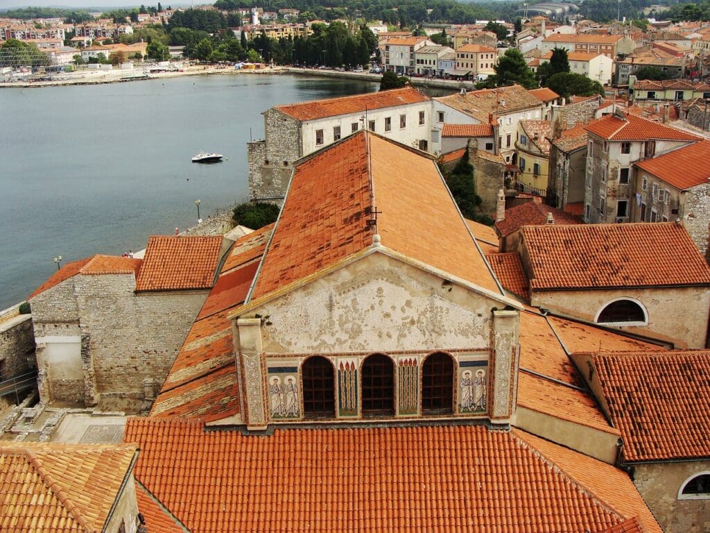 Aerial view of a coastal town in Croatia with red-tiled roofs, historic buildings, and the sparkling Adriatic Sea in the background.