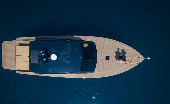 Aerial view of a luxury boat on dark blue water, with a person lying at the front, towels beside them.