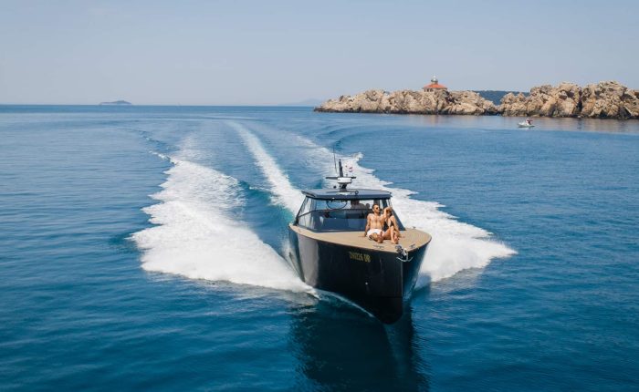 A speedboat with passengers cruises on a clear blue sea near a rocky coastline.