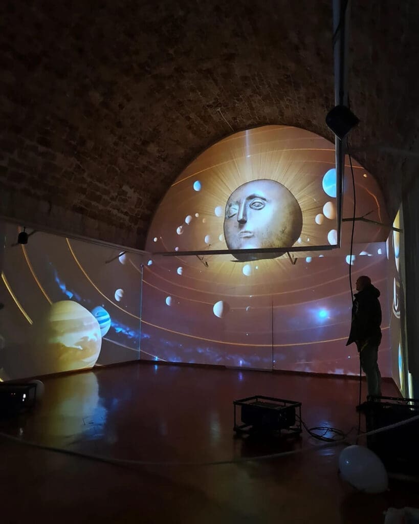 A man observes a digital art projection of a face on a planet set in space, displayed on a curved wall inside a vaulted room, reminiscent of the surreal beauty found on day trips to Dubrovnik.