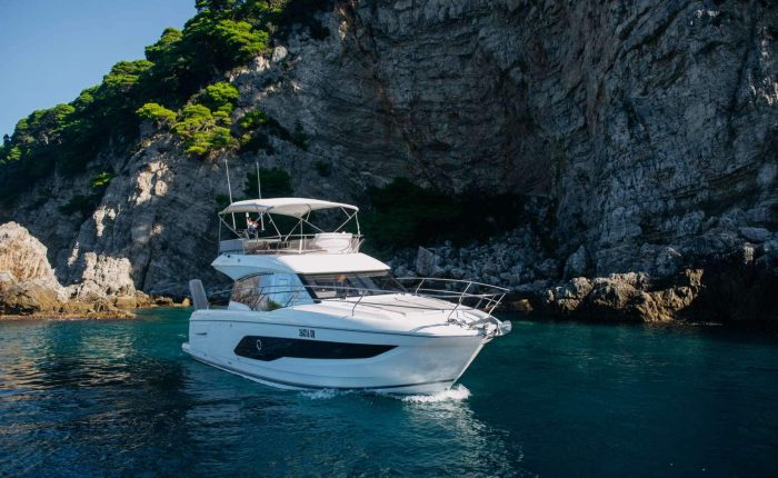 A white motor yacht floats on clear blue water near rocky cliffs with green trees.